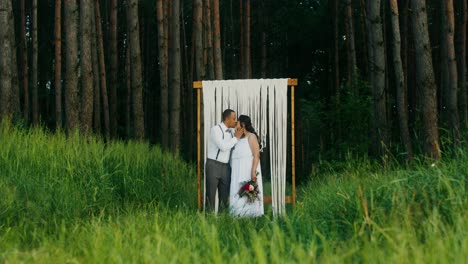 couple kissing under a wooden arch in a forest