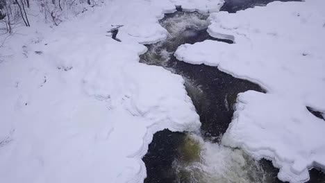 órbita aérea en cámara lenta alrededor de una pequeña cascada helada durante una tormenta de nieve de invierno