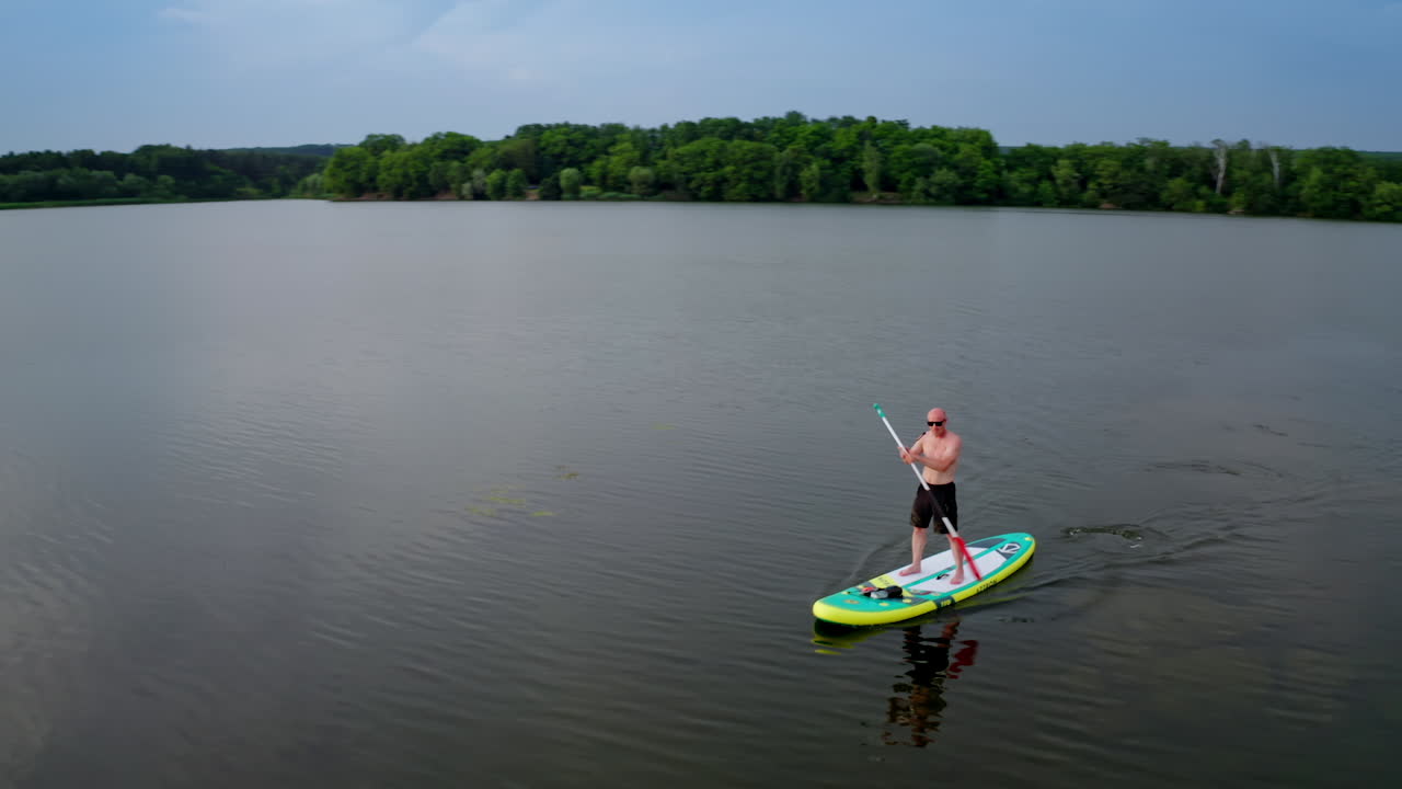 Man standing on paddle board. Aerial view of man paddling on SUP board on large river