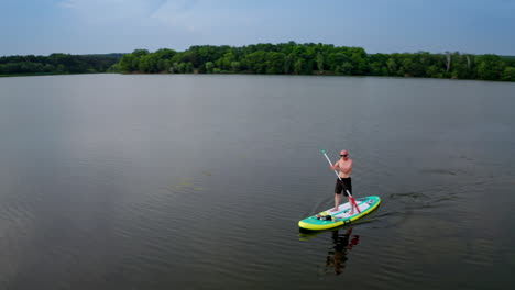 man standing on paddle board. aerial view of man paddling on sup board on large river