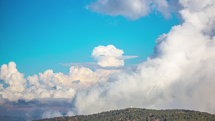 White fluffy clouds flowing above mountain landscape, time lapse view