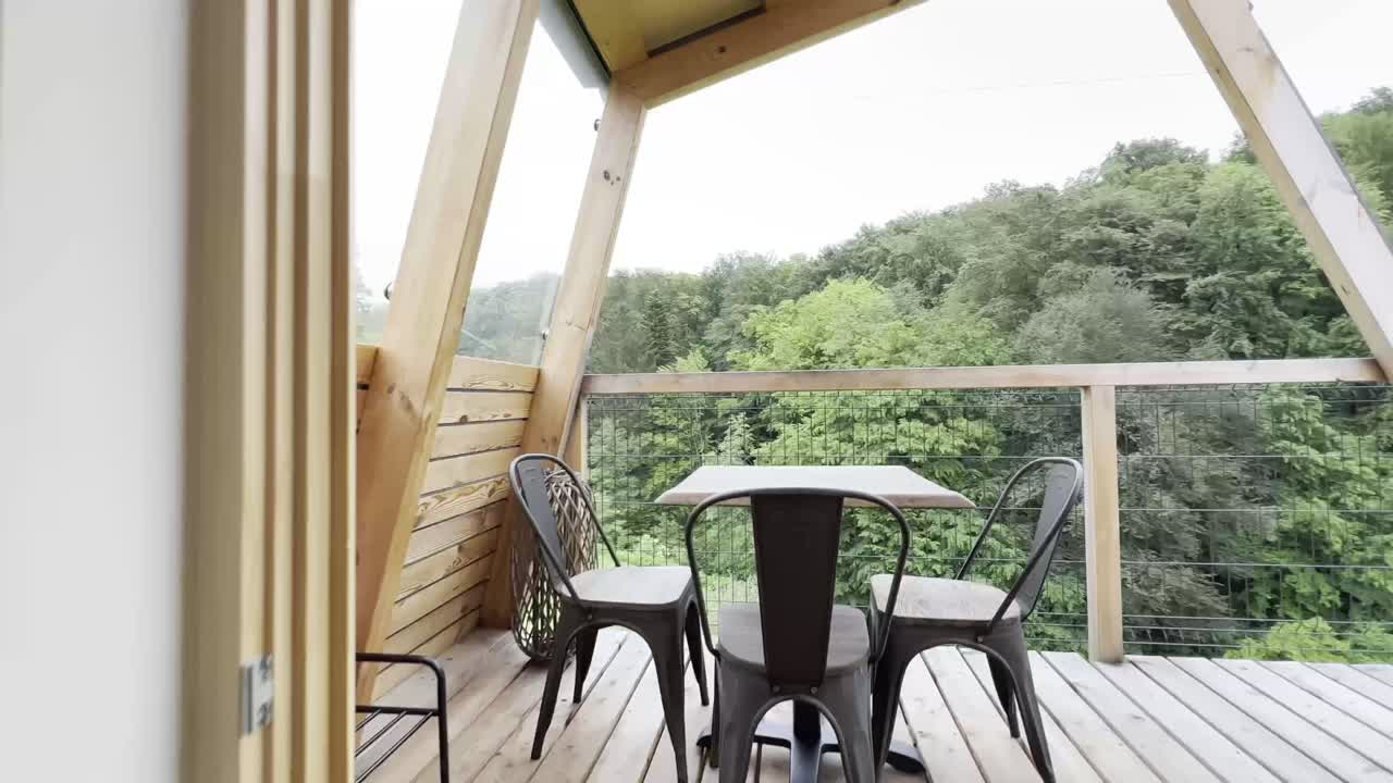 A wooden porch of a small wooden house in the mountains.  Inside a glamping house in the middle of the forest. Beautiful view to the nature through a huge glass door