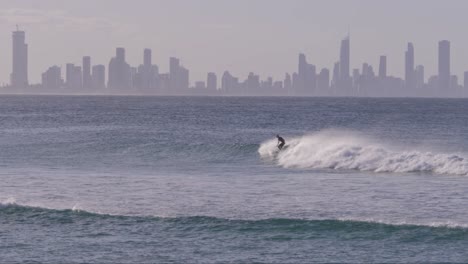 surfer riding waves at currumbin alley beach backdropped by surfers paradise skyline in fog. queensland, australia. wide shot