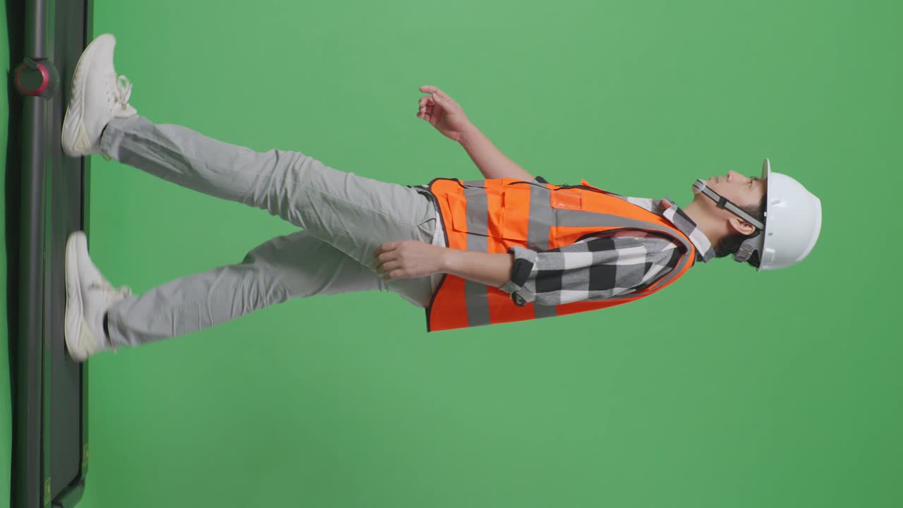 vista lateral de cuerpo completo ingeniero masculino asiático con casco de seguridad y caminando en el estudio de fondo de pantalla verde