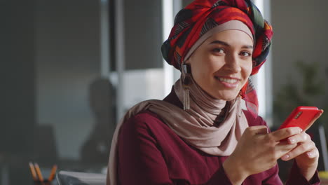 Mujer-De-Negocios-Musulmana-Usando-Un-Teléfono-Inteligente-Y-Sonriendo-A-La-Cámara