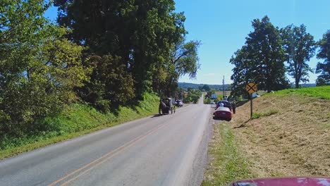 an amish horse and buggy trotting down a country road passing cars, on a beautiful sunny day