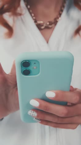 woman using a light blue phone with white nails