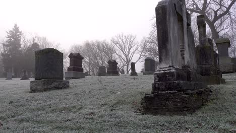 close up of spooky old tombstones in church graveyard on a foggy morning with frost on the ground 4k