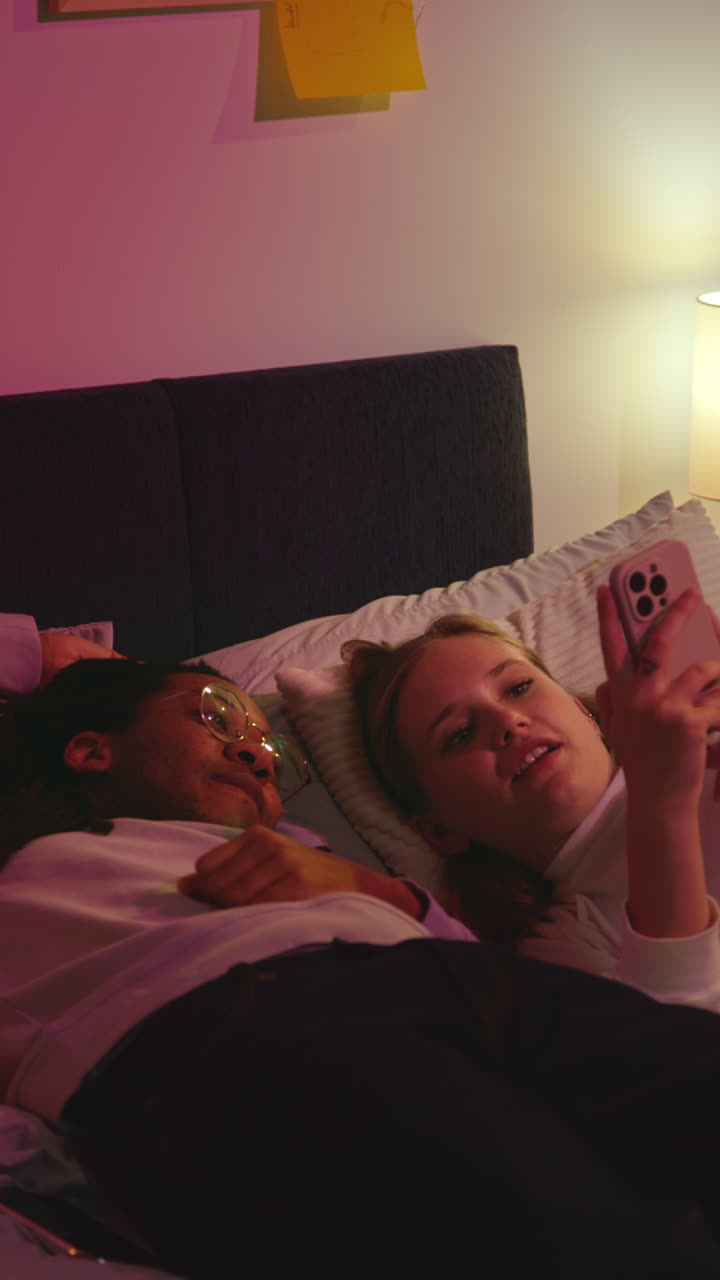 Couple laying in bed looking at phone