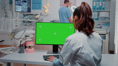 Dentist-working-with-horizontal-green-screen-on-monitor-at-desk