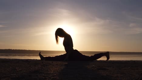 Junge-Frau-Macht-Spagat,-Yoga-Haltung-Draußen-Am-Strand.-Schöne-Silhouette-Des-Athleten.-Sonnenuntergang