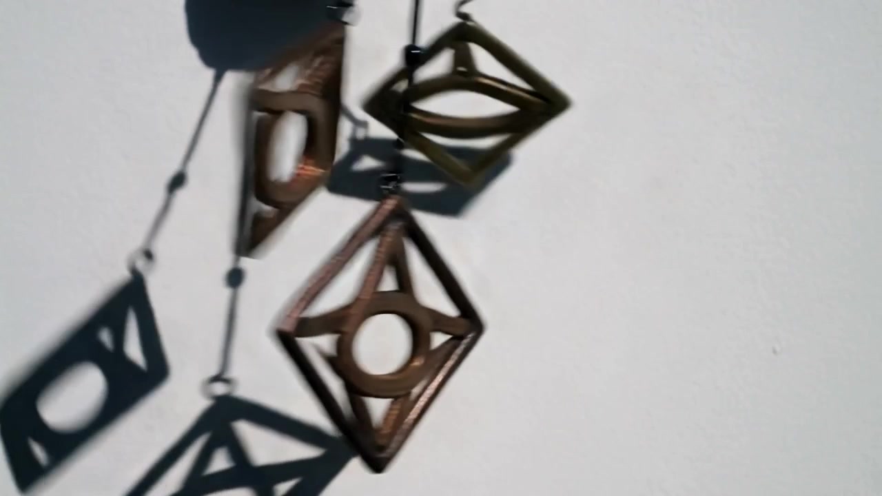 Swinging twin diamond metal pendants rotating on white wall under left sunlight, casting shadows