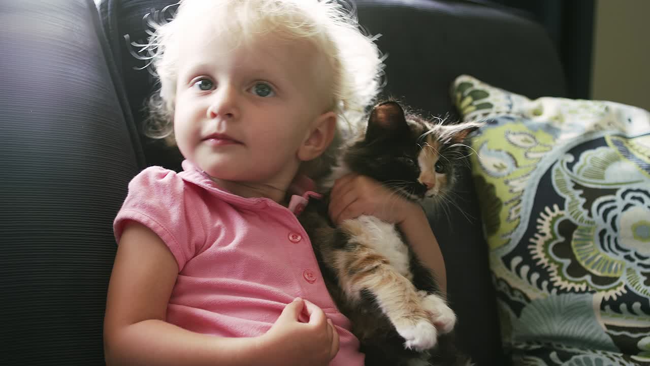 uma menina sentada no sofá segurando um gatinho e dando-lhe um abraço