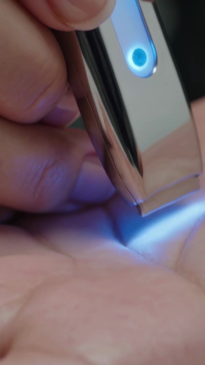 Video verticale: Accensione di un LED blu, adulto che tiene un dispositivo premendo una punta blu sul palmo in una stanza buia.