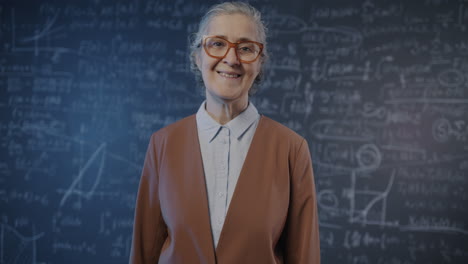 smiling teacher in front of a blackboard filled with equations