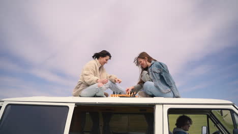 two young girls play chess on the roof of a caravan on a road lost in the middle of the countryside