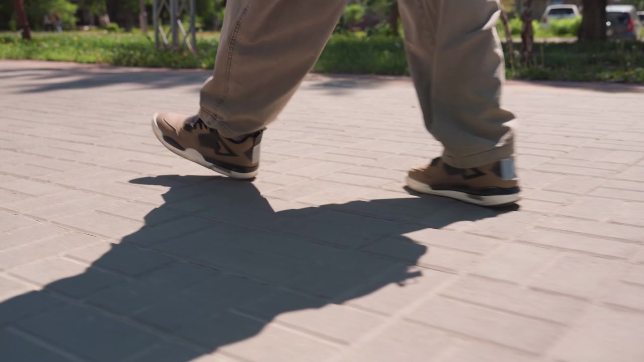 Close up of person feet and legs performing rhythmic footwork on paved ground. subject wears light brown pants and casual sneakers with shadows visible beneath them throughout sequence