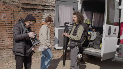 production worker setting up a camera in the street and other workers taking material for a recording from a van