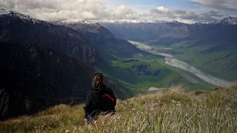 girl looking over a beautiful green valley with mountains with a river running through on a bright sunny day on a grassy hill, drifting handheld wide shot