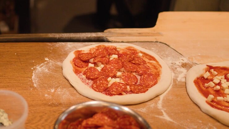 Primo piano di uno chef con guanti neri che posiziona il pepperoni sull'impasto della pizza in un ristorante