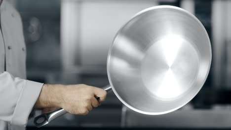 las manos del chef girando el wok en la cocina. las manos del hombre de cerca jugando con el wok.