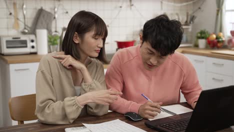 stressed asian young couple making budget plan for mortgage loans bill. the husband folds arms as his wife is showing him figure on the calculator and bills