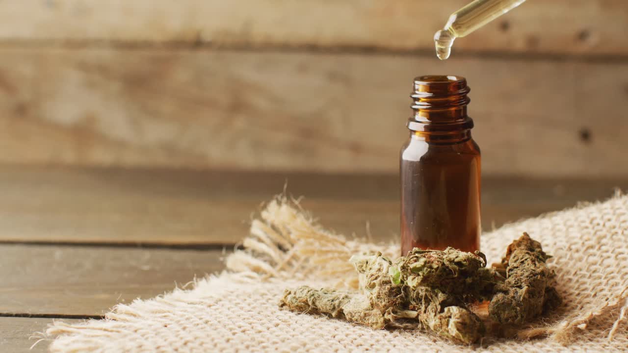 video de brotes de marihuana y una botella de extracto de cbd sobre un fondo de madera
