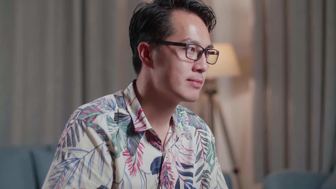 체어에 앉아 있는 아시아인 남자가 미소 짓고 엄지손가락을 올려 카메라를 향해 몸짓을 하며 집에 있는 카메라 에 있는 데스크으로 영상을 편집하고 있다.