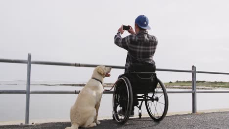 Hombre-En-Silla-De-Ruedas-Tomando-Fotografías-Del-Mar-Con-Su-Perro.