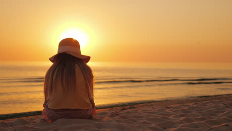 un niño está sentado en la arena de la playa mirando la puesta de sol sobre el mar
