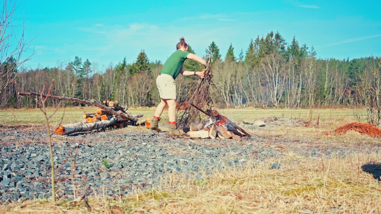 A Man Adds Kindling to an Open Fire to Char Wooden Poles - Static Shot