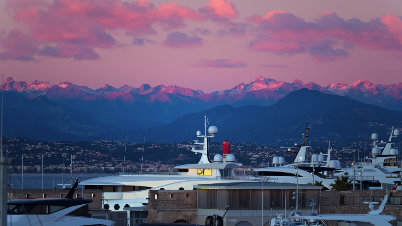 Juan-les-Pins, France - January 25, 2025: Multiple white boats docked in the harbour in Antibes with the mountains on the background at sunset