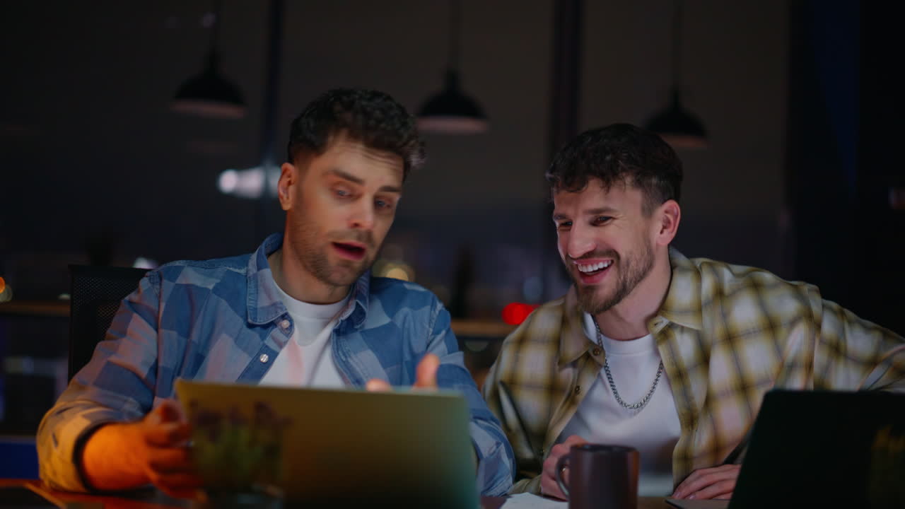 Late coworkers looking laptop discussing project at evening workplace closeup