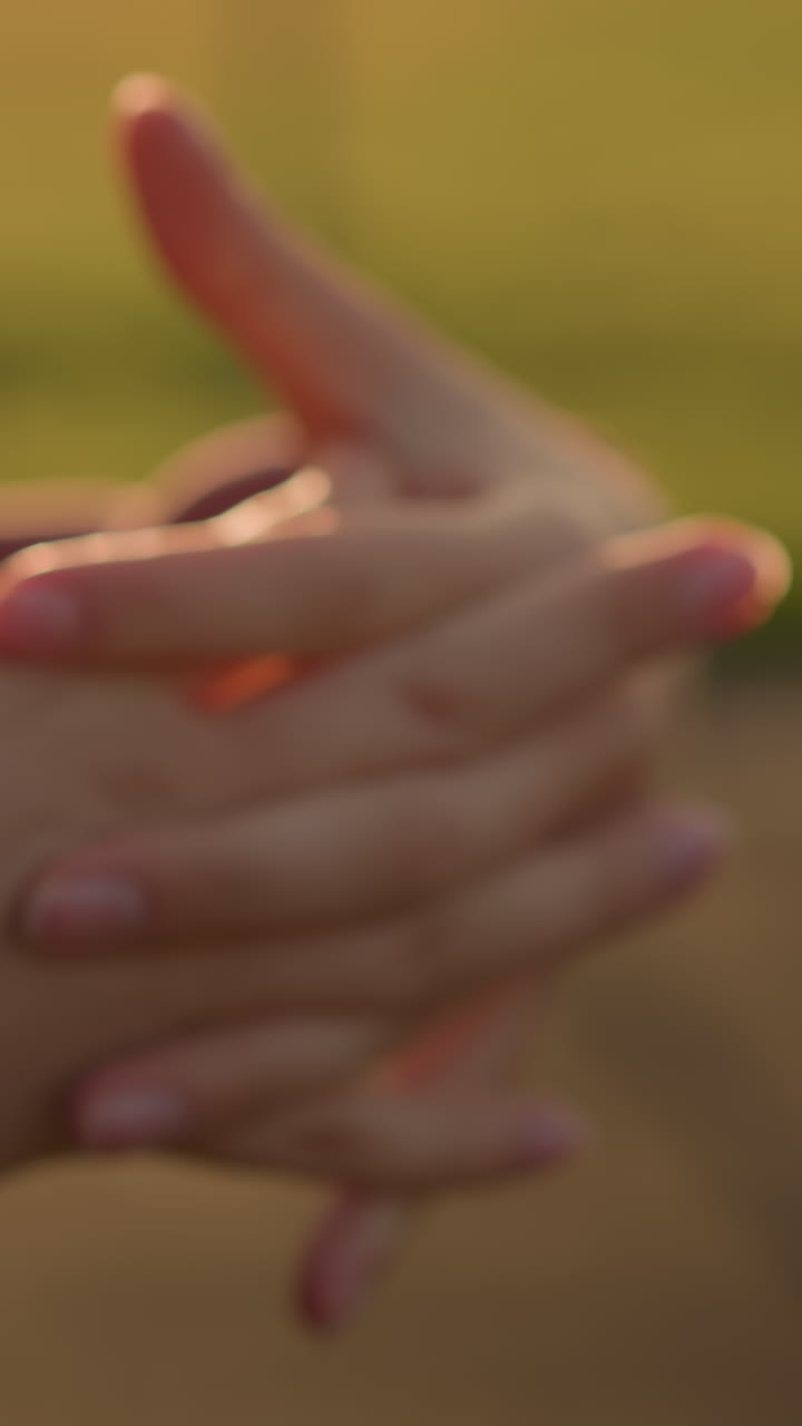 vista de mano de primer plano de una persona con ropa marrón trabajando en la muñeca con los dedos entrelazados, con la luz del sol creando un efecto brillante y un fondo verde borroso