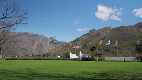 Country-flags-flapping-in-wind-at-entrance-to-property,-mountains-in-background,-rural-area,-South-Africa