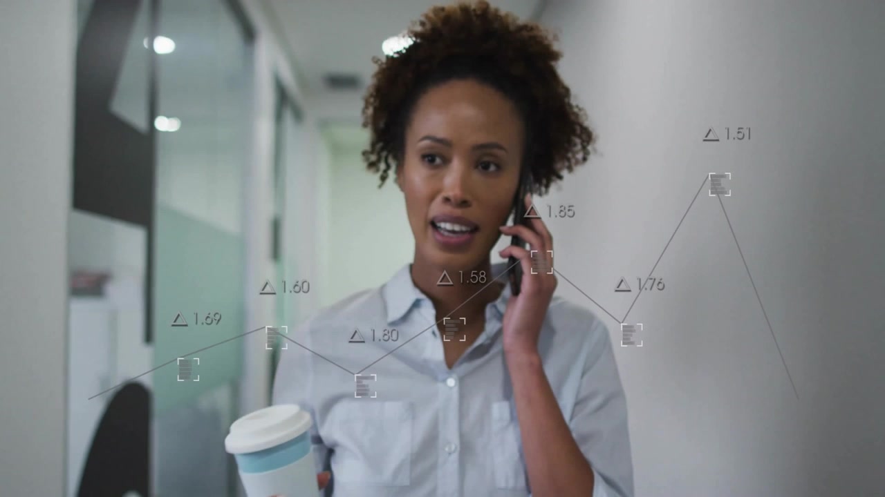 Businesswoman walking hallway holding coffee, using smartphone showing line graphs, data indicators