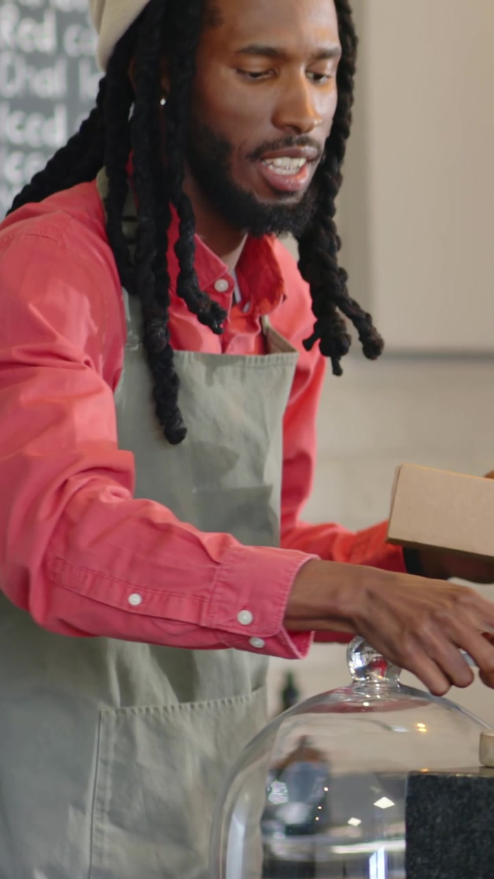 Vertical video: Lifting cloche, cafe staff in apron boxing tart into box with green tool for pickup