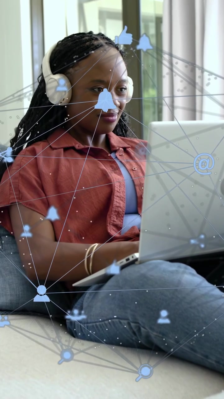 Vertical video: Remote worker woman using laptop on sofa moving upright while social icons popping