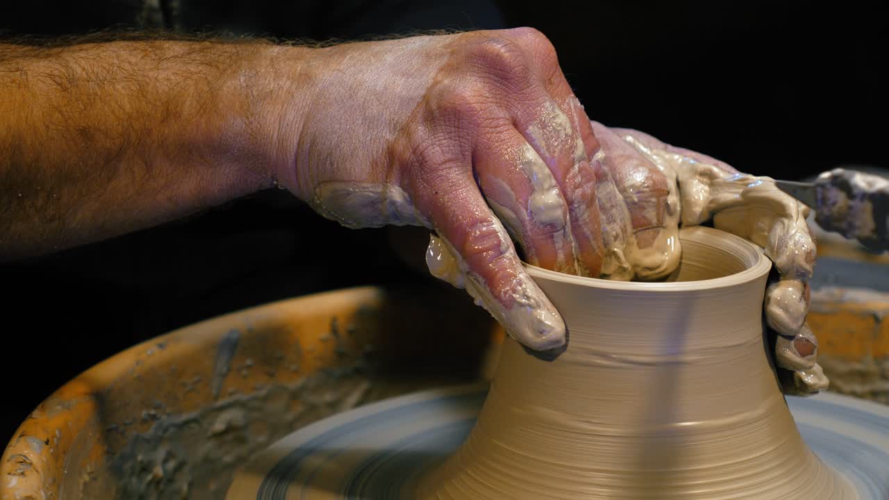 Mani di un vasaio sporche di argilla umida che lavora al tornio. Dettaglio ravvicinato delle dita di un artigiano che modella il bordo di un recipiente di ceramica con barbottina. Dettaglio del processo di artigianato artistico