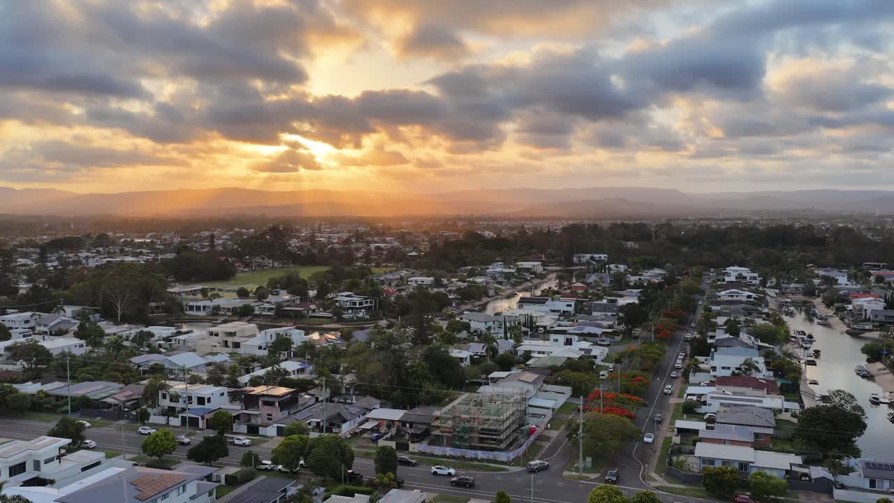 Drone glides above luxury canal homes at sunset, capturing dramatic clouds and golden light