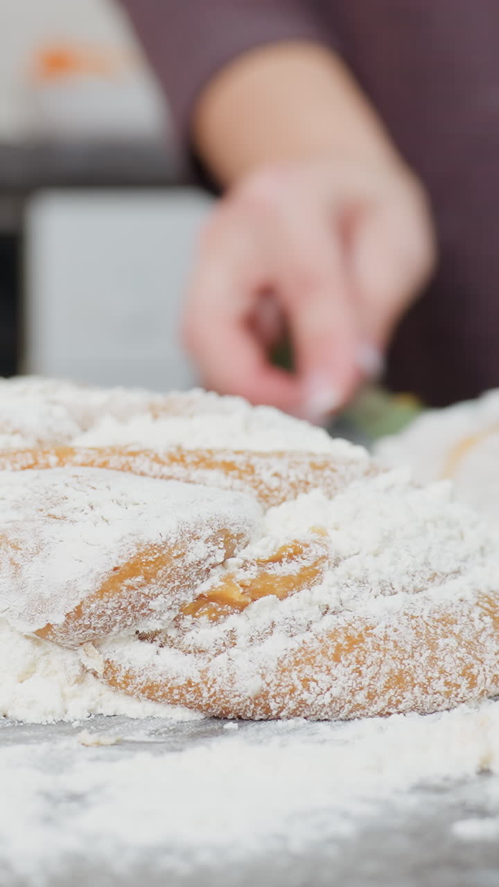 Close-up of baker in maroon cloth mixing soft dough with flour on countertop, hands kneading, folding, and blending ingredients for baking