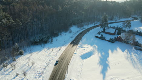 Cars-driving-on-a-black-asphalt-road-cleared-in-a-winter-wonderland-with-shadows-of-trees-streched-out-over-the-white-snow