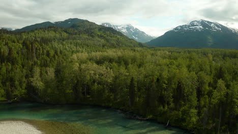Dramatic-aerial-footage-of-green-river-bend-with-high-mountain-peaks-rising-in-the-background