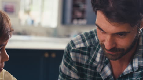 Cerca-Del-Padre-En-Casa-En-La-Cocina-En-La-Mesa-Ayudando-A-Su-Hijo-Con-La-Tarea