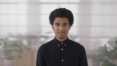 Retrato-De-Un-Joven-Hombre-De-Raza-Mixta-Confiado-Mirando-La-Cámara-Sonriendo-Orgulloso-En-El-Fondo-Del-Espacio-De-Trabajo-De-Oficina