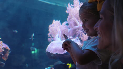 mother with little girl in aquarium looking at fish in tank excited child watching marine animals with curiosity having fun learning about sea life with mom in oceanarium