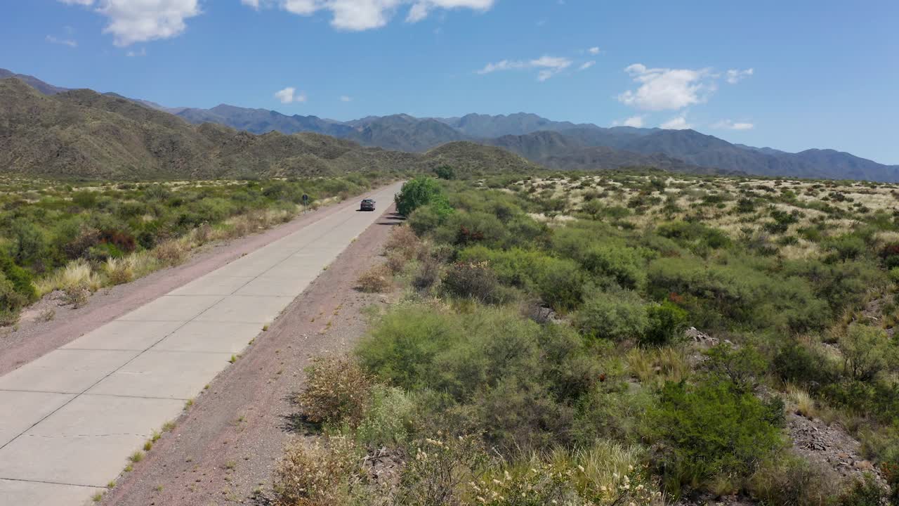 Coche circulando por una carretera larga y solitaria en un lugar árido americano