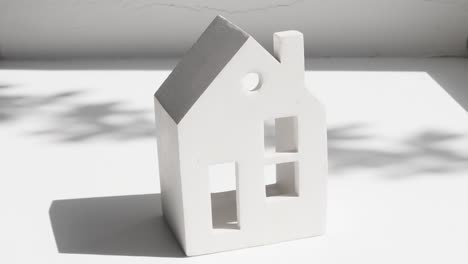 white ceramic house on a light gray background with sunlight and shade from plants.