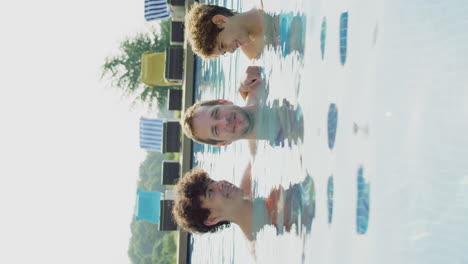 vertical video of father with sons having fun in outdoor swimming pool on summer vacation together