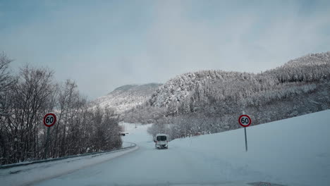 POV-video-of-a-daytime-drive-through-the-snowy-roads-of-Norway's-Western-Fjords,-surrounded-by-tall,-snow-covered-mountains-with-trees